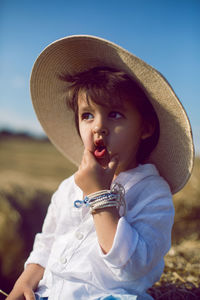 Baby boy in straw hat and blue pants sitting on a haystack in a field in autumn