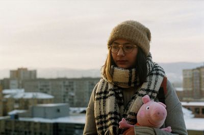 Woman with stuffed toy in city against sky during winter
