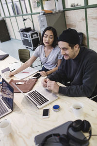 Young woman and man using laptop at desk in office