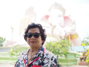 Portrait of woman wearing sunglasses against ganesha statue