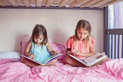 Siblings reading picture book while sitting on bed at home