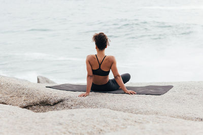 Full length of woman sitting on rock at beach