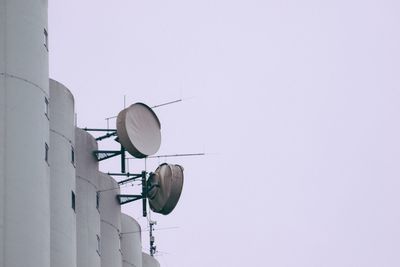 Low angle view of repeater dishes on silos against clear sky