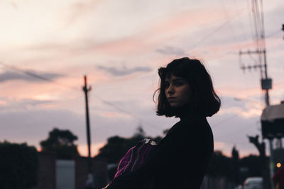 Young woman standing against sky during sunset