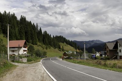 Road by trees and buildings against sky