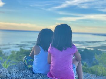Two kids watching the sunset sitting on top of the mountain overlooking the ocean. 