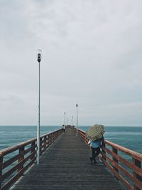 Rear view of woman with umbrella standing on pier over sea against sky