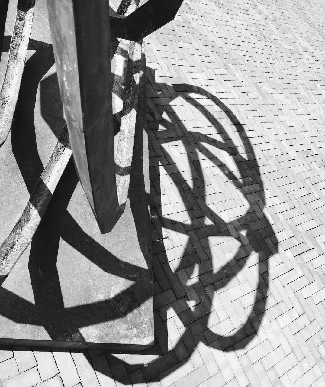 bicycle, shadow, transportation, street, high angle view, city, wheel, day, footpath, sunlight, no people, land vehicle, outdoors, mode of transportation, sidewalk, pattern, paving stone, wall - building feature, nature, road, focus on shadow