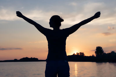 Rear view of carefree woman enjoying at the beach during summer sunset.