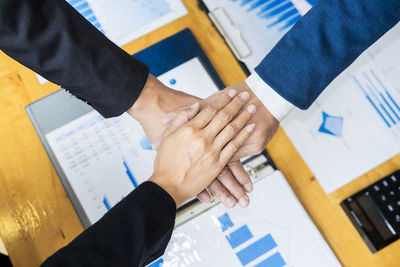 Cropped image of business people stacking hands over desk in office