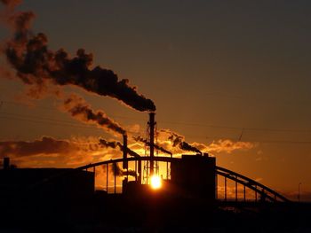 Smoke emitting from chimneys against sky during sunset