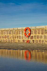 Life belt on wall at shore against blue sky