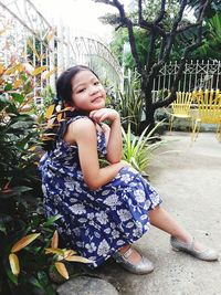 Full length portrait of girl sitting by plants at yard