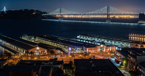 Illuminated bridge over river in city at night