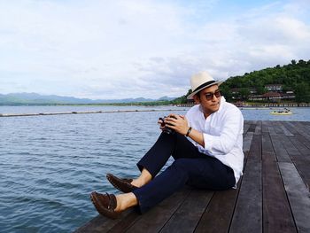 Man sitting on pier over sea against sky