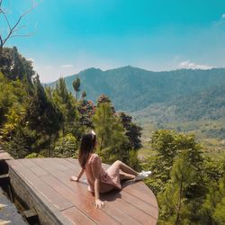 Full length of woman sitting on wooden plank against mountain