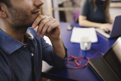 Midsection of young man sitting with hand on chin at desk in creative office