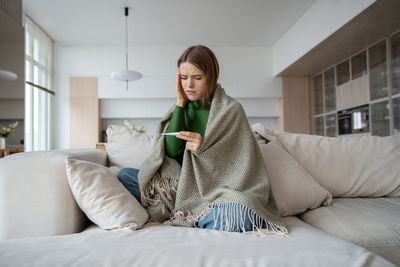 Woman feeling unwell, having symptoms of flu, virus, suffering from headache looking at thermometer