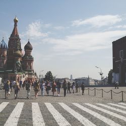 People walking in city against cloudy sky