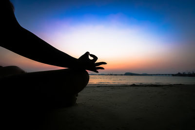 Silhouette hand on beach against sky during sunset