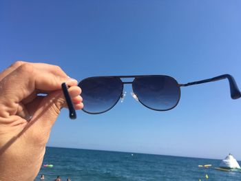 Close-up of hand holding sunglasses against clear blue sky