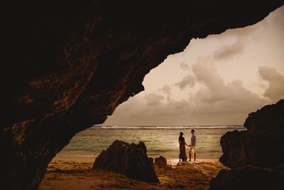 Woman standing on rock by sea against sky
