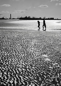 Man and woman walking on beach against sky