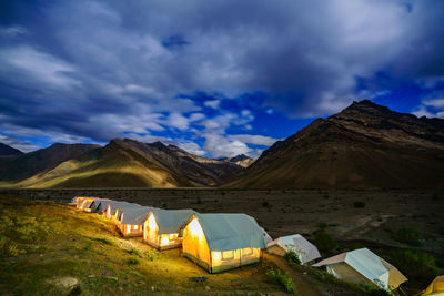 Illuminated tents by mountains against sky at dusk