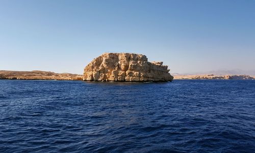 Rock formations in sea against clear blue sky