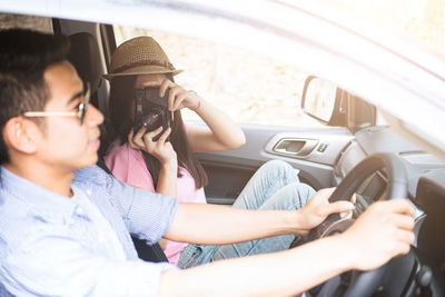 Woman photographing man while sitting in car