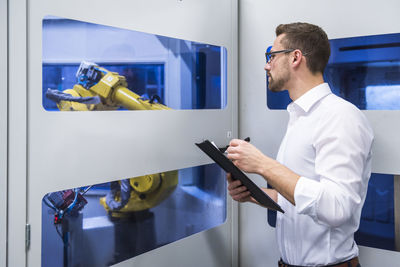 Man taking notes at robotics machine in factory shop floor