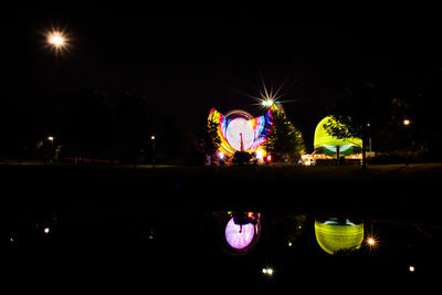 Illuminated ferris wheel in city against sky at night