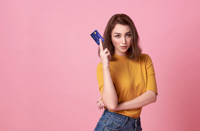 Portrait of young woman holding camera while standing against pink wall