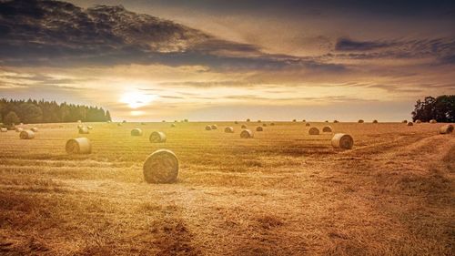 Hay bales on field against sky during sunset