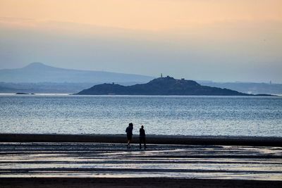 Rear view of couple sitting on sea against sky