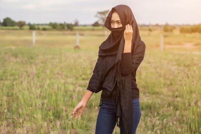 Woman wearing headscarf covering face while walking on grass