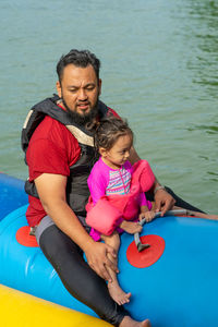 Full length of father and daughter on banana boat in water