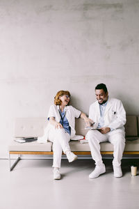 Full length of cheerful doctors sitting on sofa at hospital