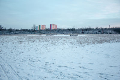 Snow covered field by building against sky