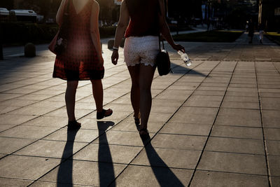 Low section of women walking on footpath in city during sunset