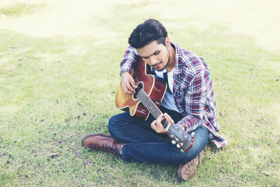 Man playing guitar while sitting on field
