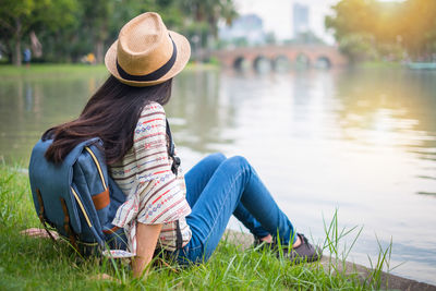Rear view of woman sitting on grass by lake