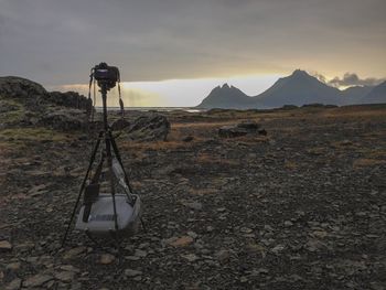 Camera with tripod on field against sky during sunset