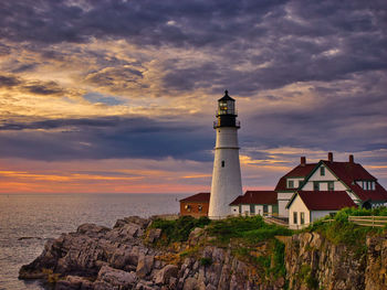 Lighthouse by sea against sky during sunset