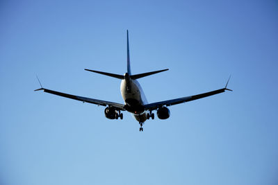 Low angle view of airplane flying against clear blue sky