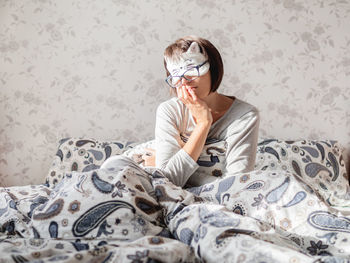 Young woman in grey pajama, glasses and sleeping mask in shape of cute sleeping cat face. 