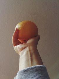 Close-up of person holding apple against wall