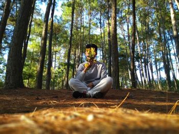 Surface level view of young man sitting against trees in forest