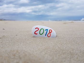 Close-up of text on sand at beach against sky