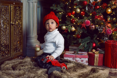 Baby boy sitting next to christmas tree on soft skin near fireplace during christmas